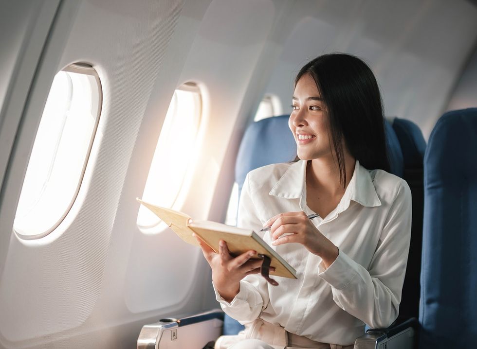 A smiling woman looks out of the window of an airplane