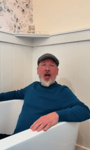 Man in teal sweater sitting in a bathtub.