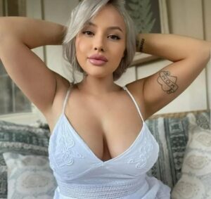 Portrait of a woman with gray hair wearing a white dress and a "Mom" tattoo.