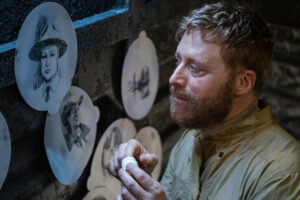 Harry (Alan Tudyk) looks sadly at sketches of Elizabeth Bowen’s Deputy Liv Baker and Corey Reynolds’ Sheriff Mike Thompson in season 4 of Resident Alien
