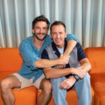Two men embracing on an orange couch.