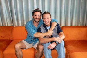 Two men embracing on an orange couch.