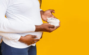 Cropped of pregnant couple holding baby shoes over yellow background