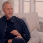 Screenshot of a man in a navy jacket sitting on a couch during an ABC interview.