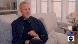 Screenshot of a man in a navy jacket sitting on a couch during an ABC interview.