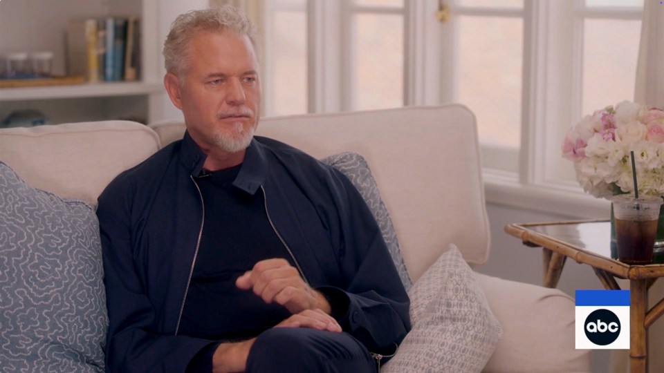 Screenshot of a man in a navy jacket sitting on a couch during an ABC interview.