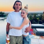 Gavin Rossdale and his girlfriend, Xhoana Xheneti, embracing by a pool at sunset.