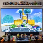 A TV set with a game on it, small figures lined up on a shelve above and a table top below.