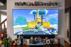 A TV set with a game on it, small figures lined up on a shelve above and a table top below.