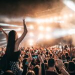 A woman sits on a man's shoulders at a crowded concert.