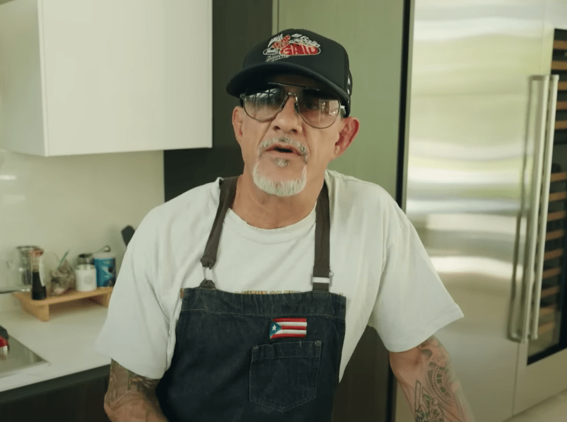Screenshot of a man wearing a chef's apron and baseball cap.