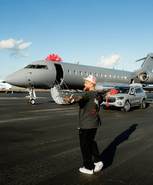 Man standing on tarmac next to a private jet and luxury SUV, both with pink bows.