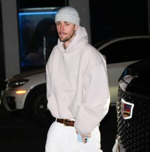 Justin Bieber wearing a light-colored hoodie, knit hat, and white pants in New York City.