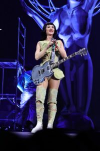 Katy Perry performing onstage with a guitar.