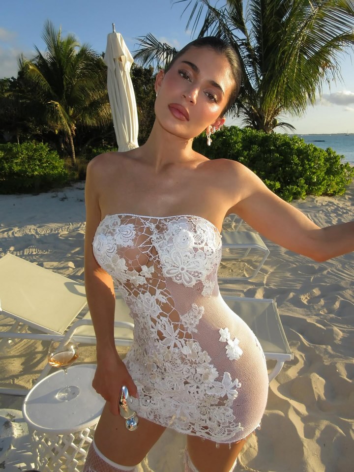 Kylie Jenner on a beach wearing a white lace dress.