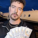 MrBeast holds a spread of cash against a private jet in the background.