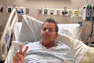 Man in hospital bed giving peace sign and middle finger.