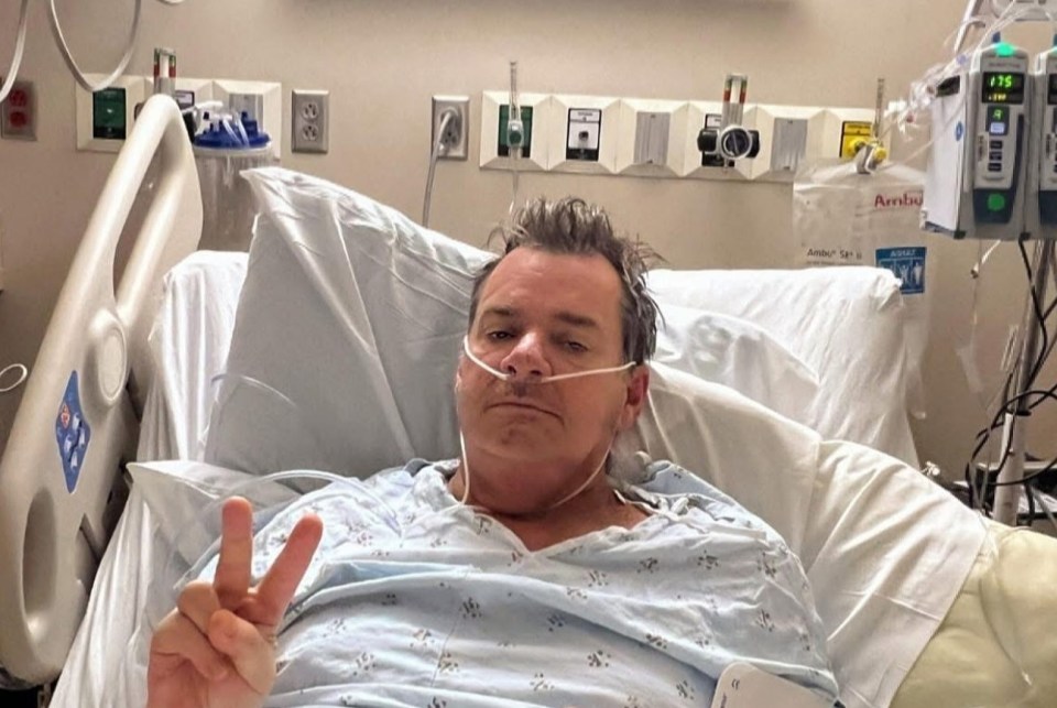 Man in hospital bed giving peace sign and middle finger.