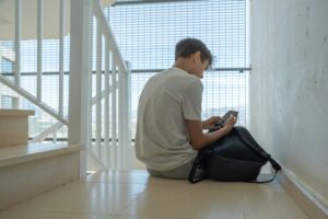 A sad teenage boy looks at his phone.