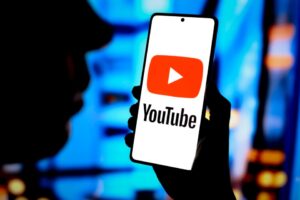 Photo illustration of a hand holding a smartphone displaying the YouTube logo.