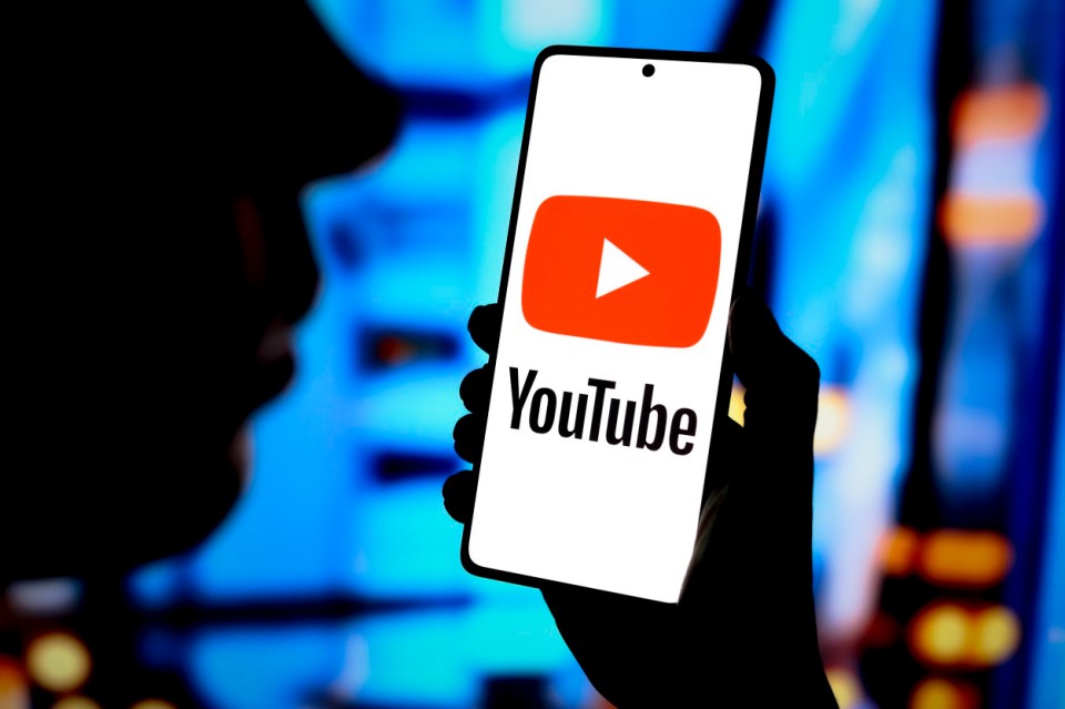 Photo illustration of a hand holding a smartphone displaying the YouTube logo.