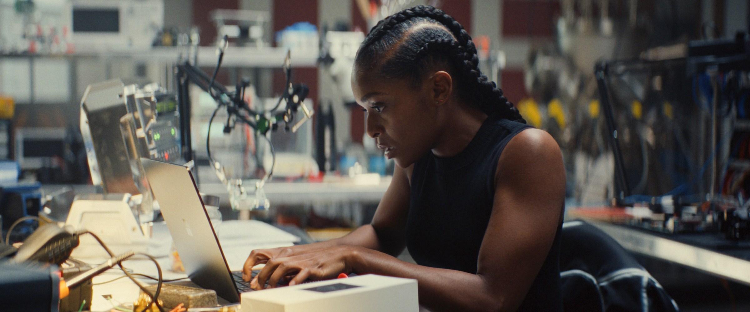 Dominique Thorne as Riri Williams works on a laptop in a robotics lab in Ironheart.