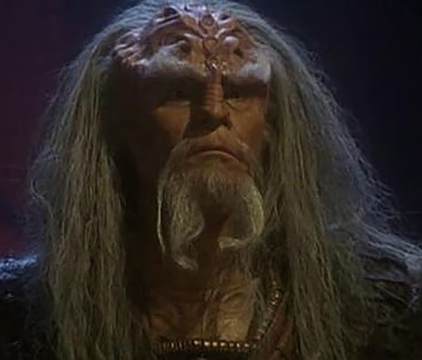 Close-up of an older man with long gray hair and elaborate headpiece.