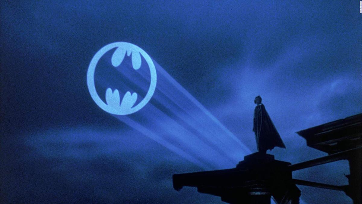 Batman looks at the Batsignal shining in the night sky