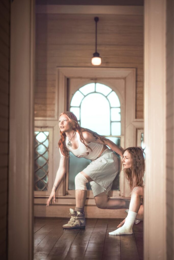 Rhian Teasdale and Hester Chambers of Wet Leg crouch walk across a hallway.