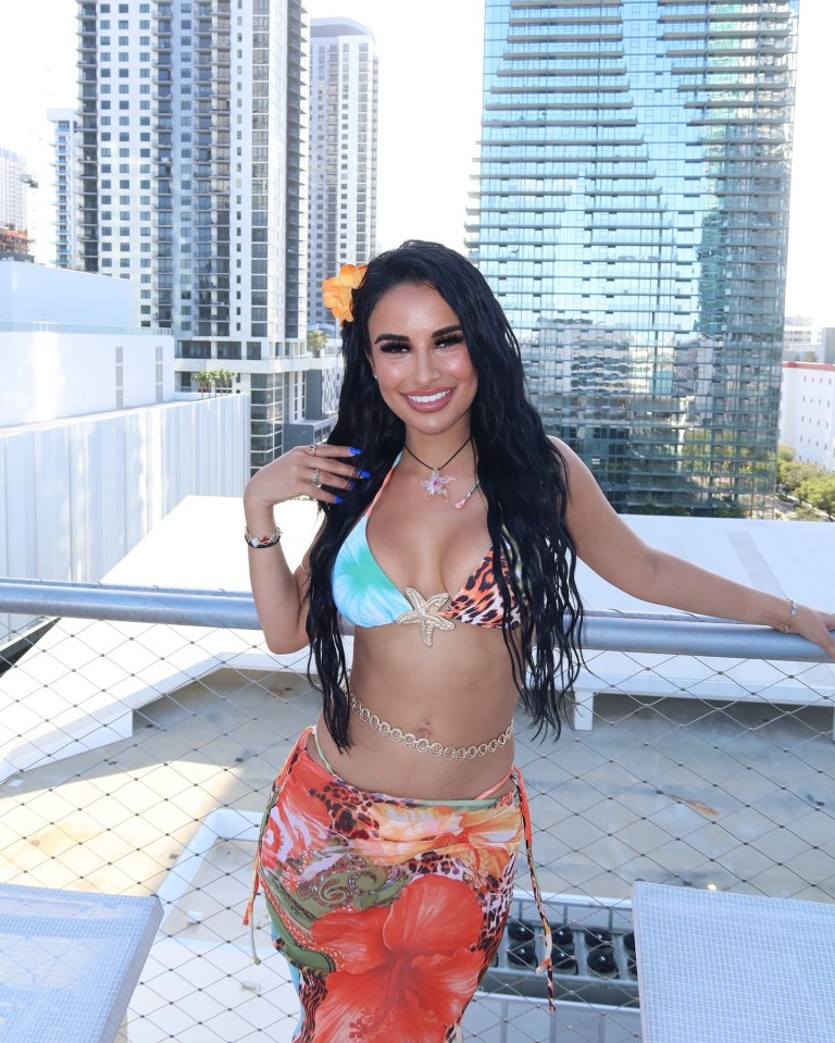 Woman in a swimsuit on a balcony overlooking city buildings.