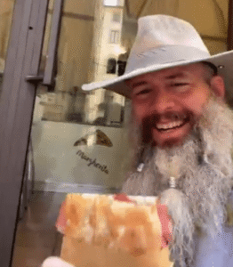 Smiling man in a hat eating pizza.