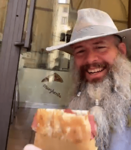 Smiling man in a hat eating pizza.