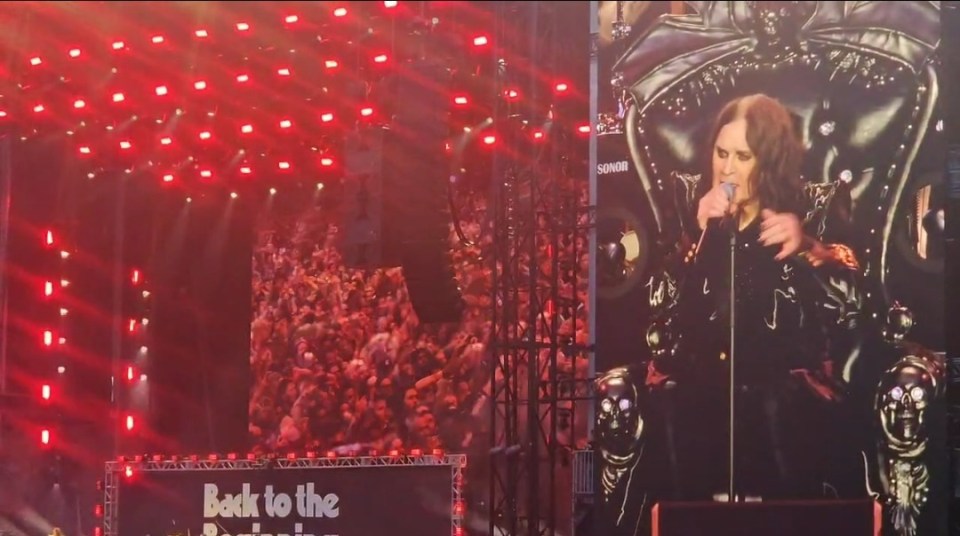 Screenshot of a performer on stage singing into a microphone while sitting on a throne.