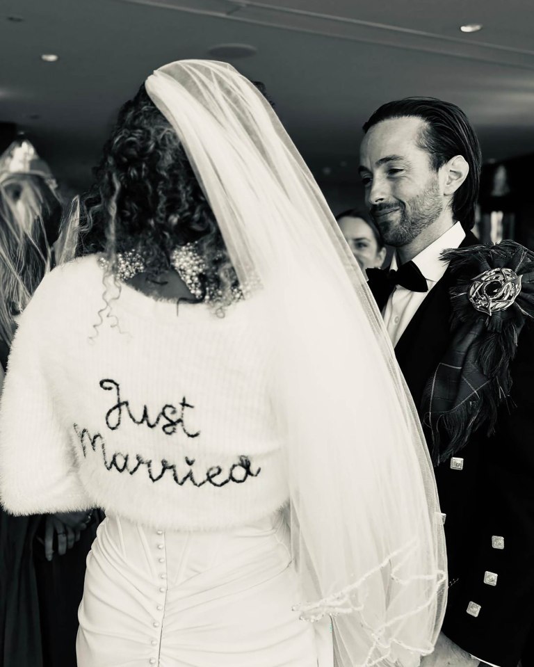 Black and white photo of a bride and groom on their wedding day.  The bride's sweater says "Just Married."