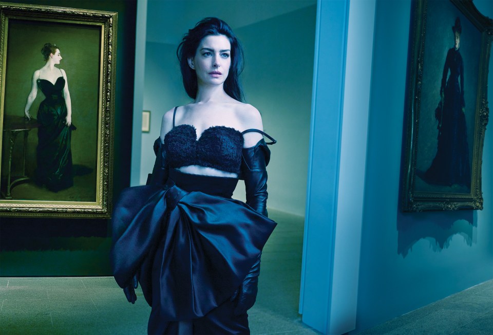 Anne Hathaway in a dark Givenchy outfit, posing in an art gallery.