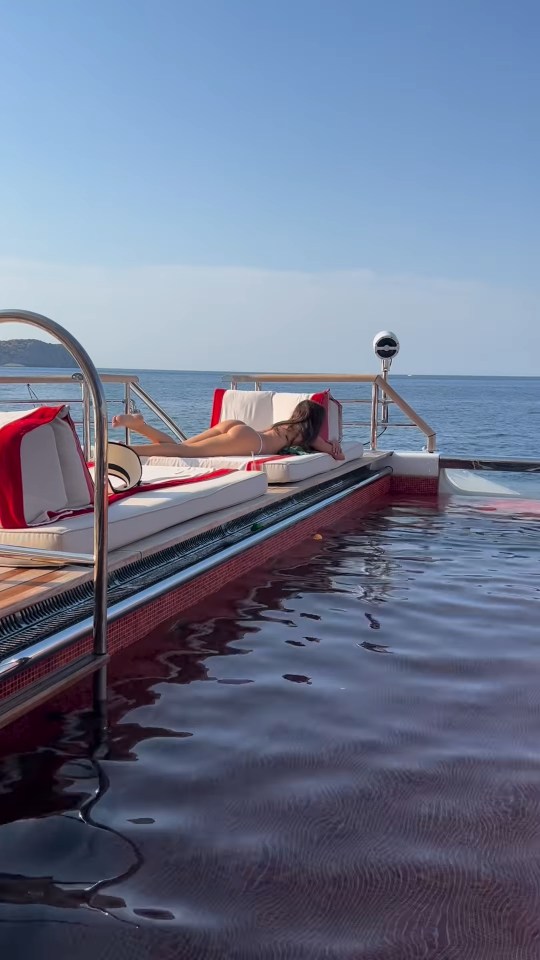 Woman sunbathing in a tiny bikini on a yacht's pool deck.