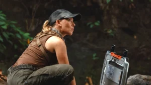 Scarlett Johansson in a baseball cap kneeling down in the jungle in Jurassic World Rebirth