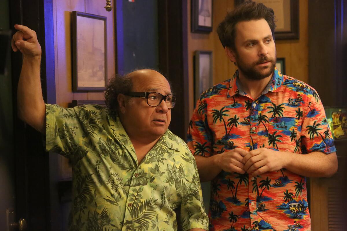 A short man in a green hawaiian shirt stands next a man in an orange hawaiian shirt.
