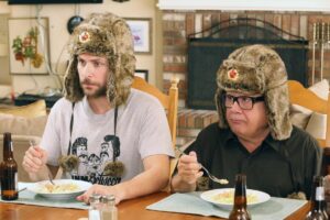 Two men in brown fur trapper hats sitting at a table eating scrambled eggs.