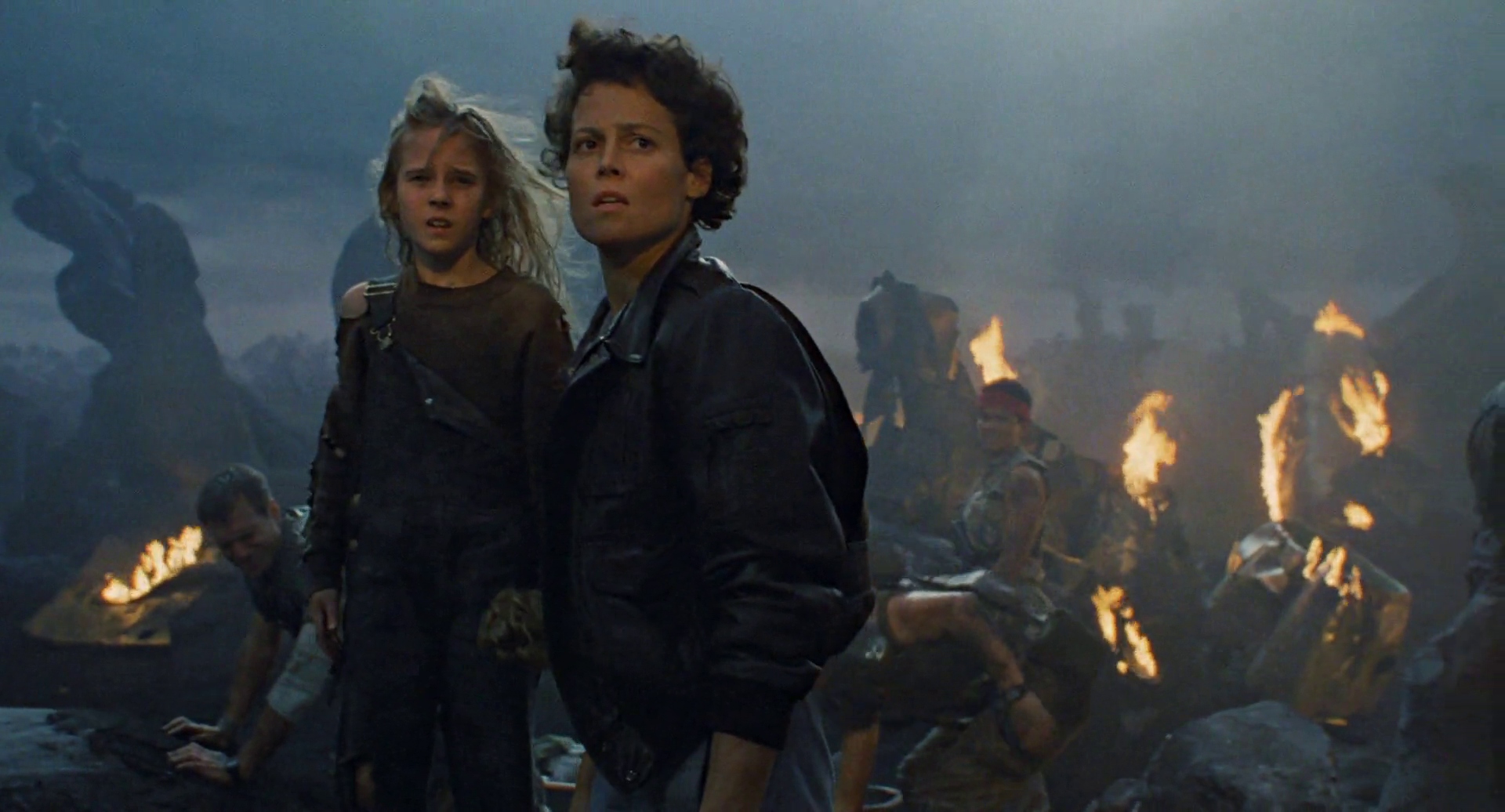 (L-R) Carrie Henn and Sigourney Weaver as Newt and Ellen Ripley surrounded by wreckage, fire, and wounded colonial marines in Aliens.