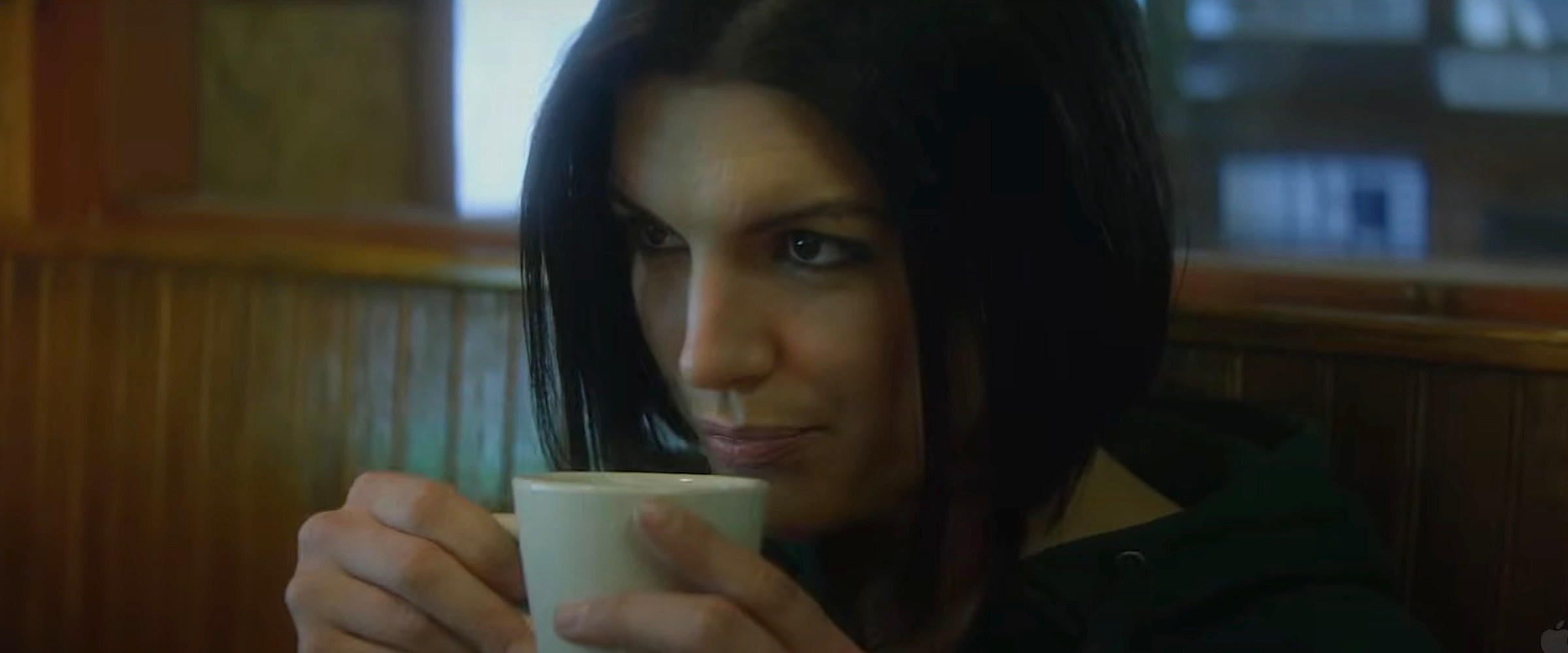 Gina Carano in Haywire holds a white mug of coffee up to her lips and smirks