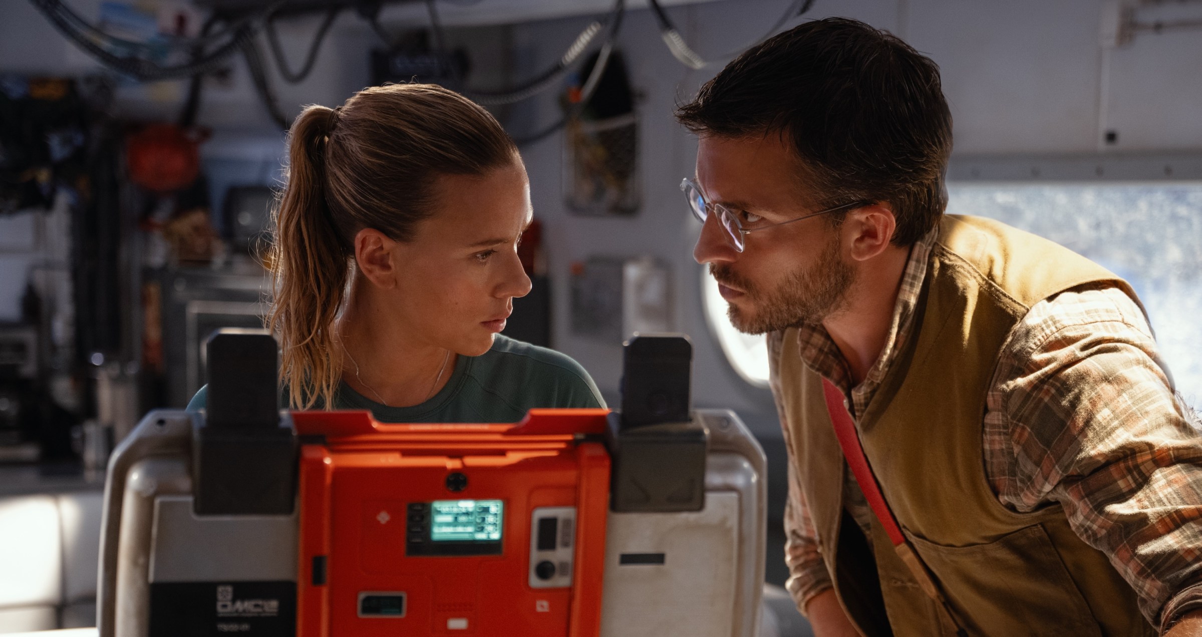 Scarlett Johansson and Jonathan Bailey, faces close together over an open high-tech briefcase, in Jurassic World Rebirth