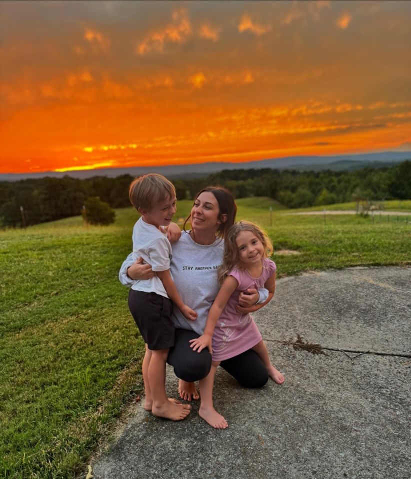 Woman hugging two young children at sunset.