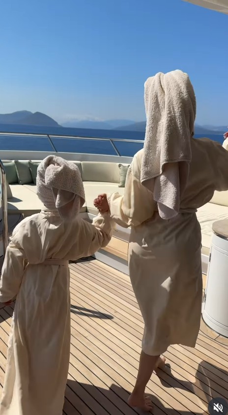 Two people in bathrobes holding hands on a yacht deck.