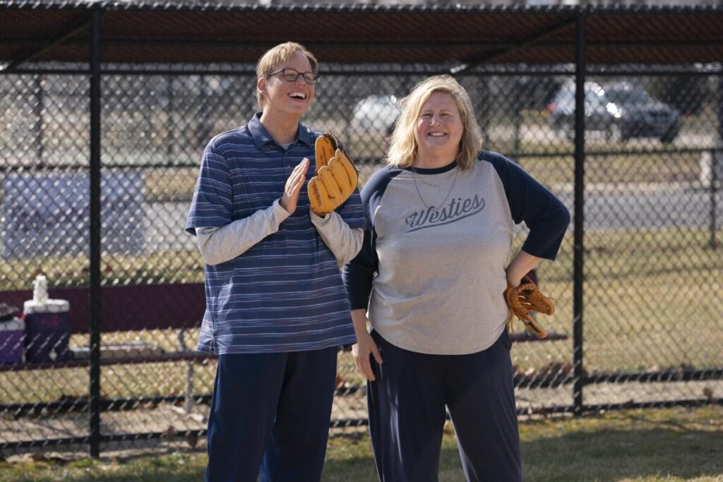 A man with a baseball glove stands next to woman on a field.
