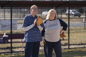 A man with a baseball glove stands next to woman on a field.
