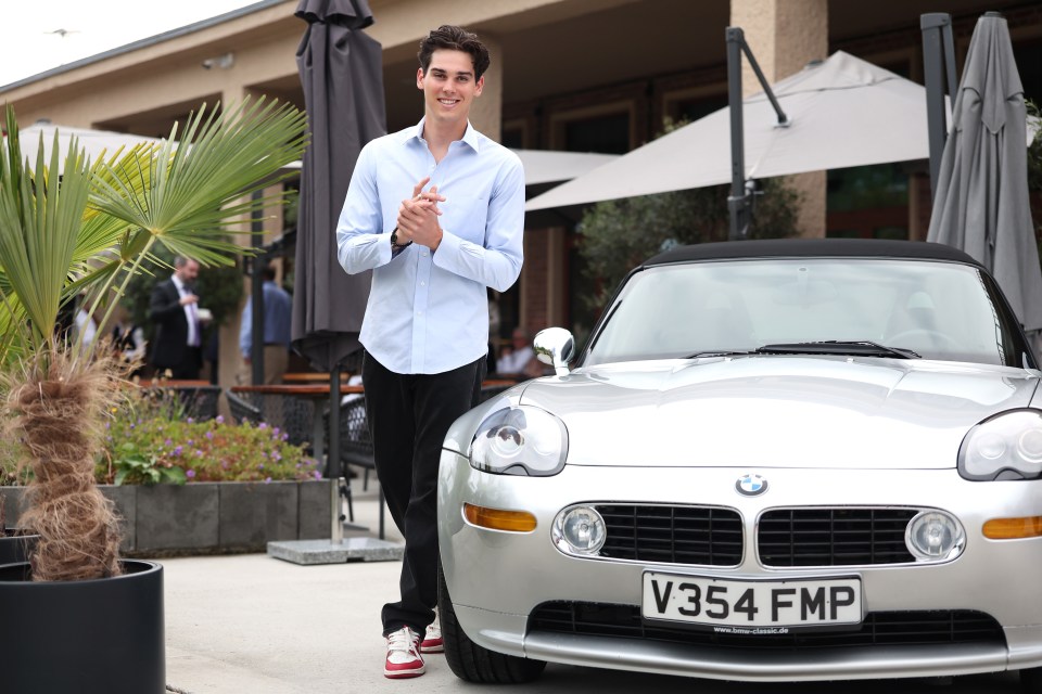 Paris Brosnan standing next to a silver BMW Z8.