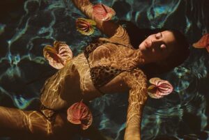 Woman in leopard print bikini submerged in pool with flowers.