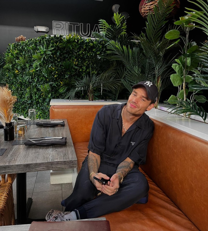 Liam Payne sitting on a brown leather bench at a restaurant.