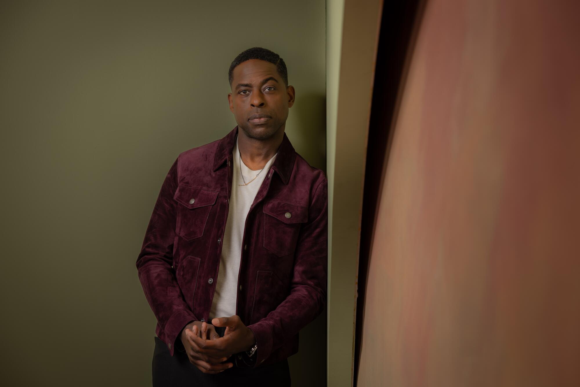 Sterling K. Brown leans against the wall and looks at the camera